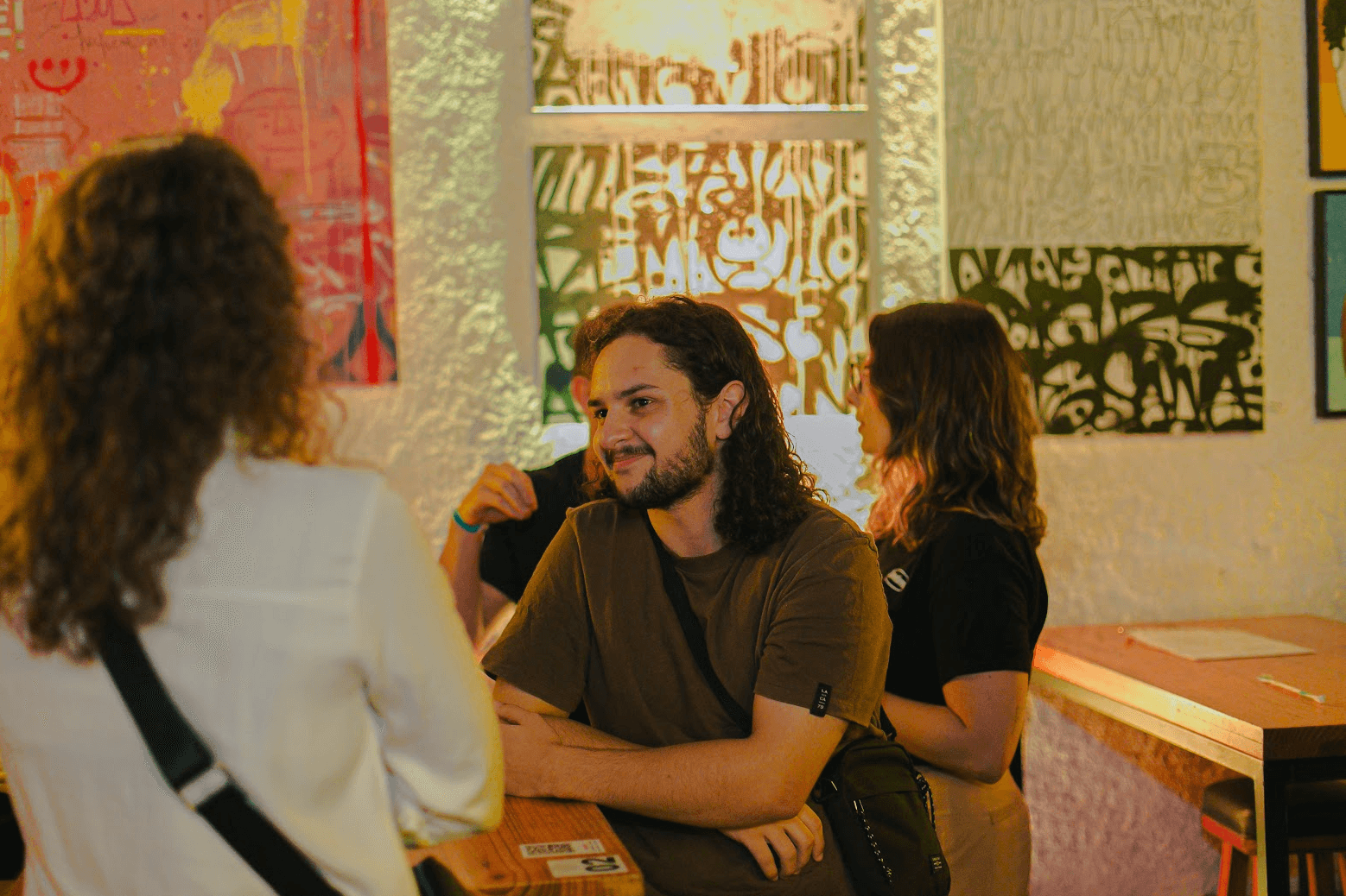 Jonathan in brown t-shirt, with long curly hair in a orange envoriment looking at a woman with white shirt and curly hair.